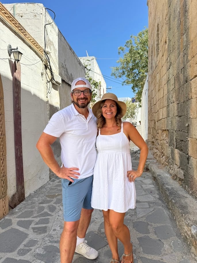 Man and woman wearing white clothing and hats standing together in a narrow stone alley on a sunny day